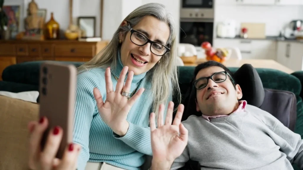 Disabled man with mother waving at phone